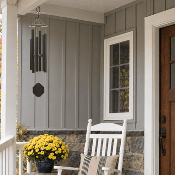 Melody of the Heart textured copper wind chime beside a white rocking chair on a gray porch.