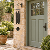 Song of Solomon textured copper wind chime in a stone courtyard beside a sage-green door.