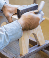 Craftsperson's hands brushing finish onto a wooden rocking toy in a workshop.